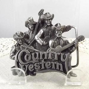 K&ouml;nnte beinhalten: Silberne G&uuml;rtelschnalle mit einer Gruppe von vier Country-Musikern, die Instrumente spielen. Die Schnalle ist mit den Worten "Country Western" graviert.