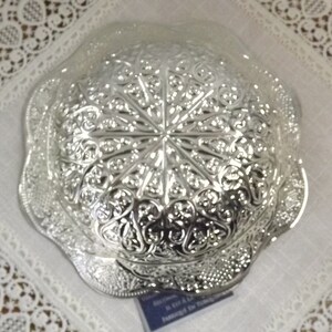 Puede incluir: Un cuenco de plata con un dise&ntilde;o intrincado en relieve. El cuenco tiene un borde festoneado y una base circular.