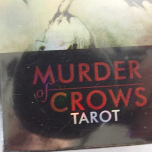 May include: A black box with the text "Murder of Crows Tarot" in red and white lettering.
