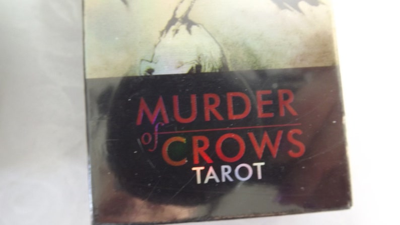May include: A black box with the text "Murder of Crows Tarot" in red and white lettering.