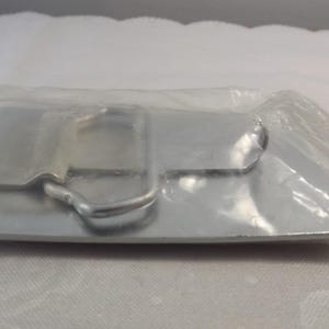 May include: A silver metal belt buckle with a simple design. The buckle is packaged in a clear plastic bag.