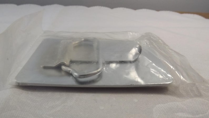 May include: A silver metal belt buckle with a simple design. The buckle is packaged in a clear plastic bag.