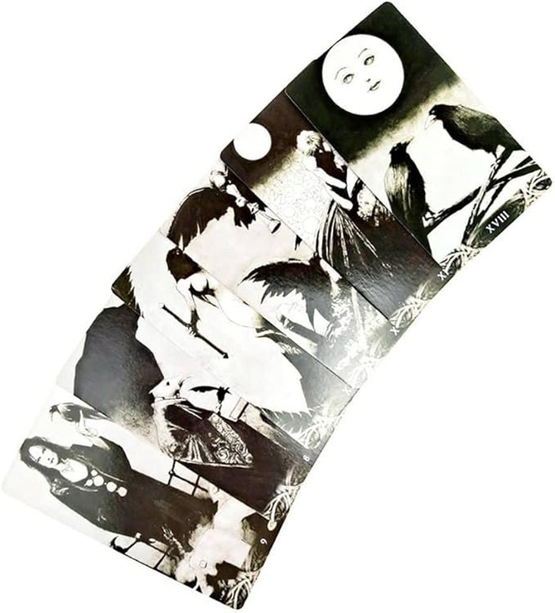 May include: A set of black and white tarot cards with illustrations of people and ravens. The cards are arranged in a fan shape, with the top card showing a full moon and the number XVIII.