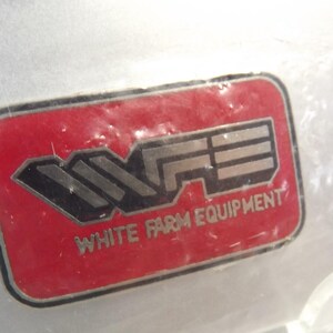 May include: A red and silver logo with the letters "WFE" and the text "White Farm Equipment" underneath.