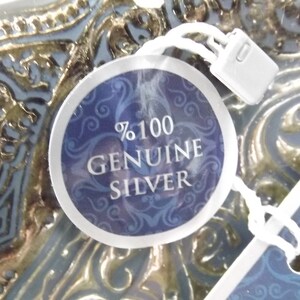 Puede incluir: Primer plano de una etiqueta de plata con fondo azul y letras blancas que dicen "100% GENUINE SILVER".
