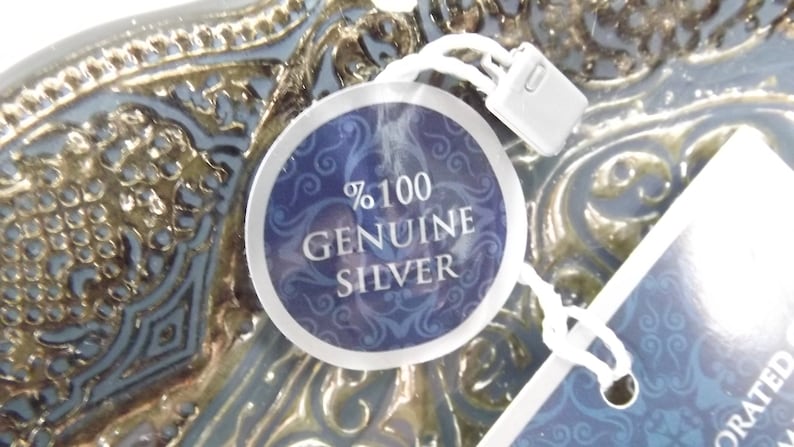 Puede incluir: Primer plano de una etiqueta de plata con fondo azul y letras blancas que dicen "100% GENUINE SILVER".