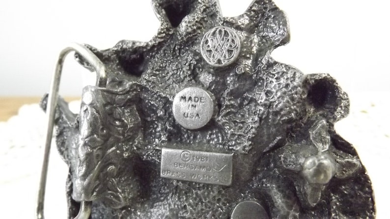 K&ouml;nnte beinhalten: Eine silberne G&uuml;rtelschnalle mit einem detaillierten Drachenmotiv. Die Schnalle ist mit "Made in USA" und "C 1981 BERGAMO BRASS WORKS" gekennzeichnet.