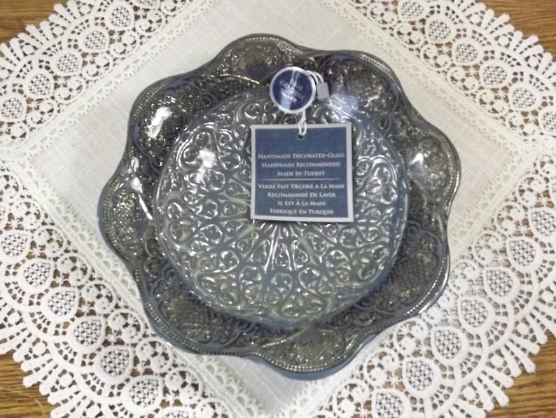 Puede incluir: Dos platos de vidrio azul con un intrincado dise&ntilde;o en relieve. Los platos est&aacute;n decorados a mano y se recomienda lavarlos a mano. El texto de la etiqueta dice: "Vidrio decorado a mano Lavado a mano recomendado Hecho en Turqu&iacute;a"