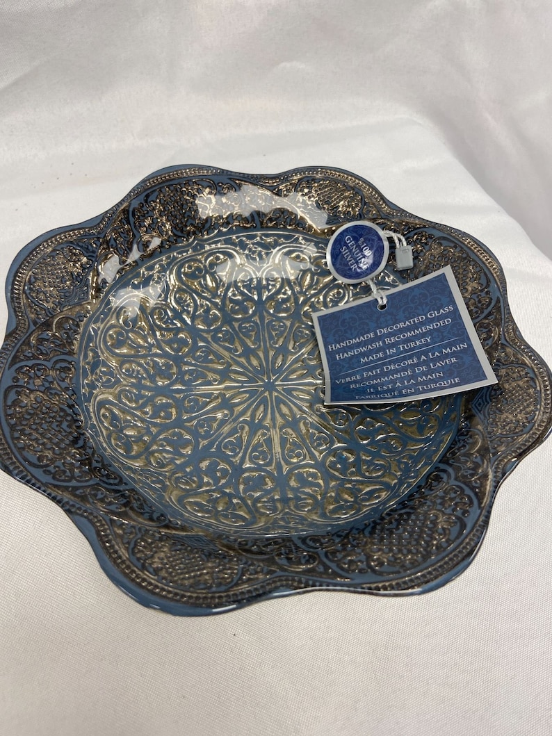 Puede incluir: Un cuenco de vidrio decorativo azul y dorado con un dise&ntilde;o intrincado. El cuenco est&aacute; hecho a mano y se recomienda lavarlo a mano. La etiqueta dice "Genuine Silver" y "Hecho en Turqu&iacute;a".