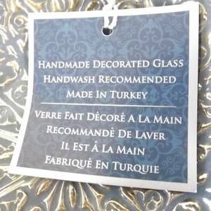 Puede incluir: Un plato de vidrio decorativo azul y dorado con una etiqueta blanca que dice en negro: "Handmade Decorated Glass Handwash Recommended Made in Turkey Verre Fait D&eacute;cor&eacute; A La Main Recommand&eacute; De Laver Il Est &Agrave; La Main Fabriqu&eacute; En Turquie".
