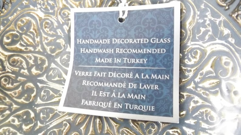 Puede incluir: Un plato de vidrio decorativo azul y dorado con una etiqueta blanca que dice en negro: "Handmade Decorated Glass Handwash Recommended Made in Turkey Verre Fait D&eacute;cor&eacute; A La Main Recommand&eacute; De Laver Il Est &Agrave; La Main Fabriqu&eacute; En Turquie".
