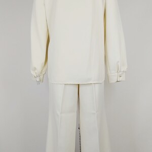 Peut inclure: Un costume blanc avec une veste &agrave; manches longues et un pantalon &agrave; jambes larges. La veste est brod&eacute;e de fleurs et d'un papillon au dos.