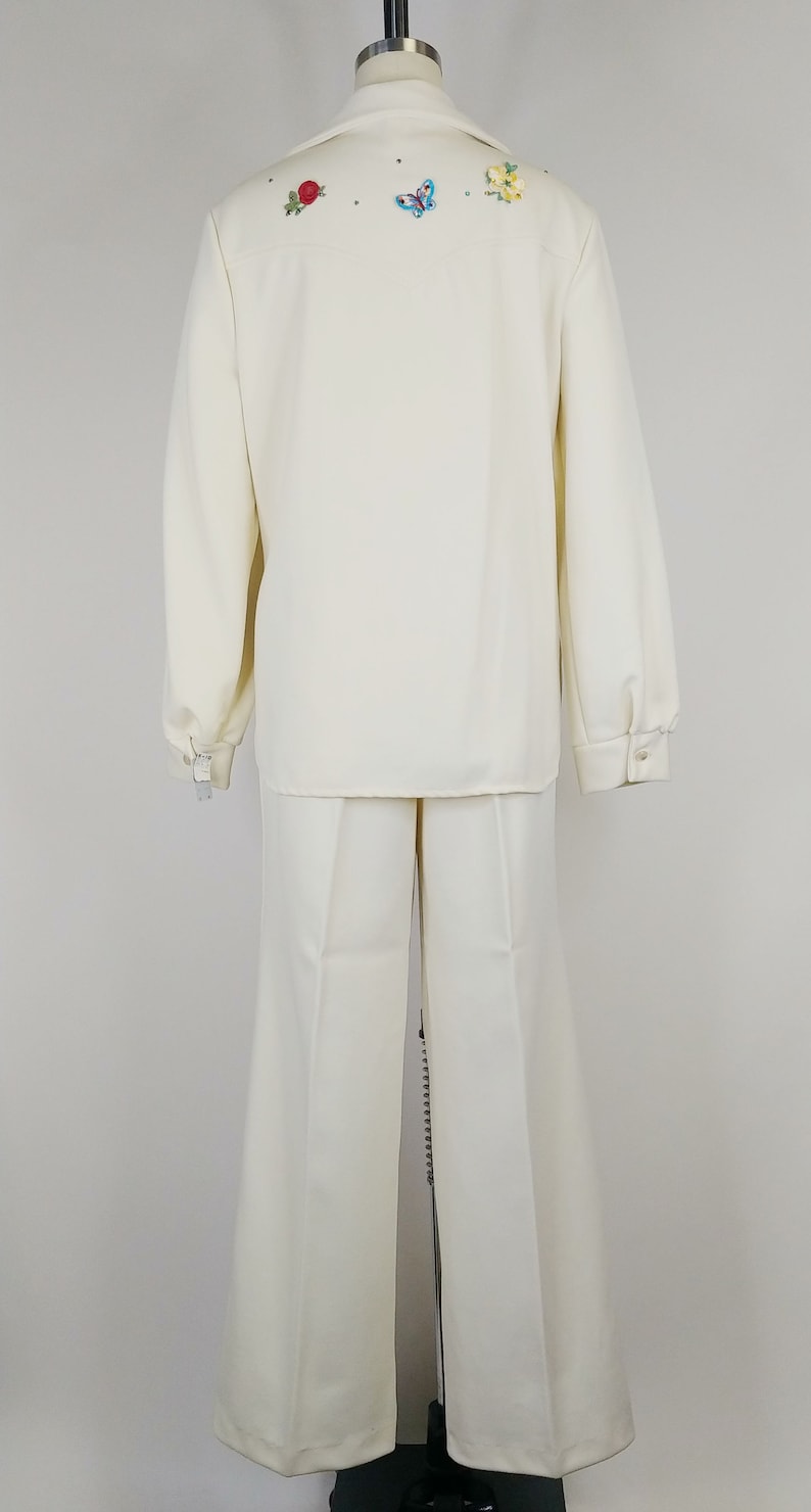 Peut inclure: Un costume blanc avec une veste &agrave; manches longues et un pantalon &agrave; jambes larges. La veste est brod&eacute;e de fleurs et d'un papillon au dos.