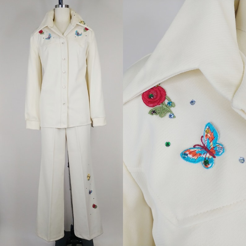 Peut inclure: Un tailleur blanc compos&eacute; d'une veste &agrave; manches longues boutonn&eacute;e et d'un pantalon &agrave; jambes larges. Le tailleur est d&eacute;cor&eacute; de fleurs et de papillons brod&eacute;s dans des tons de rouge, bleu, vert et jaune.