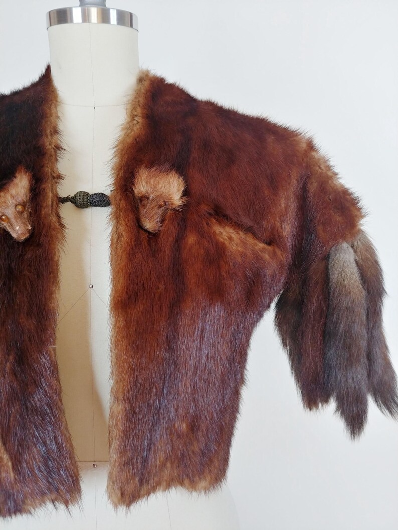 May include: A vintage brown fur jacket with a dark clasp closure. The jacket features a rich, reddish-brown color with varying shades and textures. The sleeves end in a darker, fur trim.