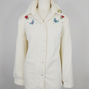 Peut inclure: Une chemise blanche &agrave; manches longues boutonn&eacute;e avec des papillons et des fleurs brod&eacute;s sur le col et les &eacute;paules.