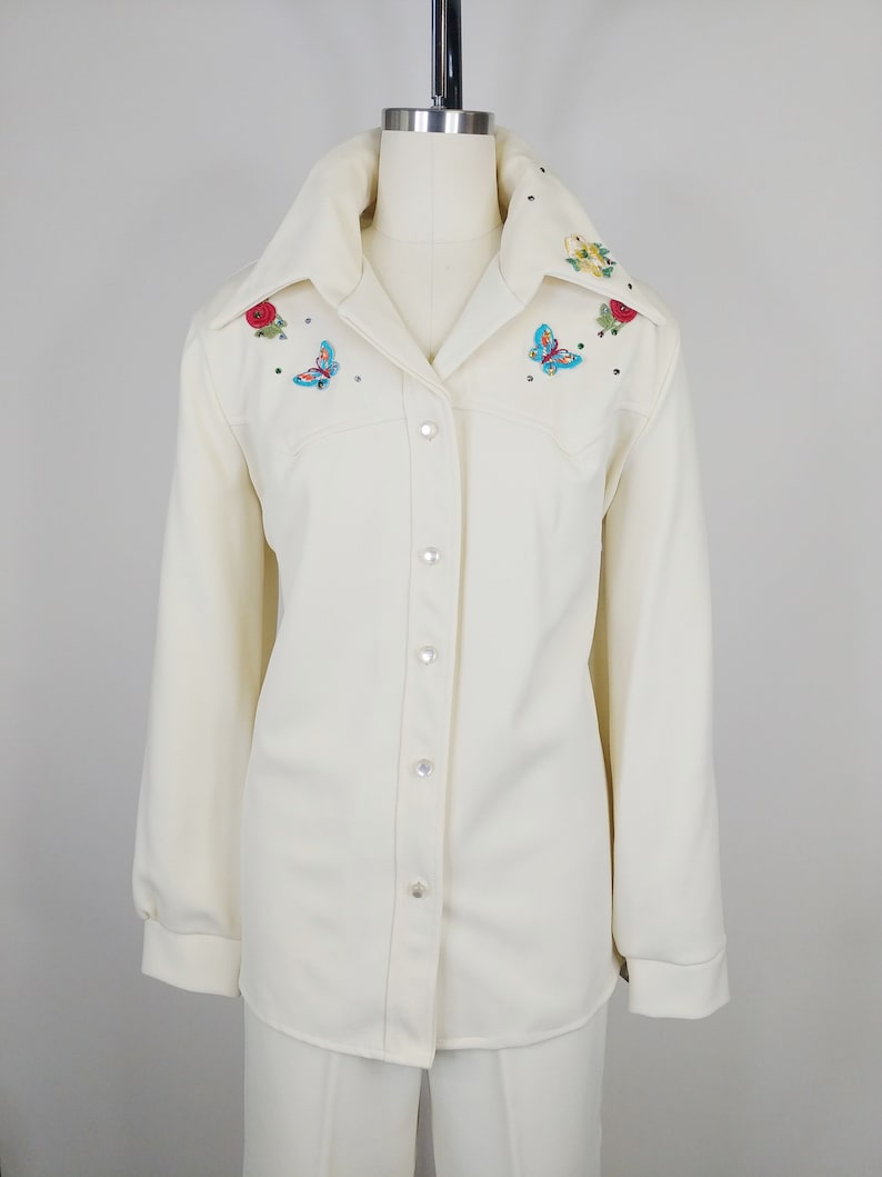 Peut inclure: Une chemise blanche &agrave; manches longues boutonn&eacute;e avec des papillons et des fleurs brod&eacute;s sur le col et les &eacute;paules.