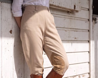 May include: A white button-down shirt with long sleeves and beige high-waisted equestrian breeches featuring tan suede knee patches, paired with tall brown leather riding boots. The word Vintage is printed in white in the bottom right corner.