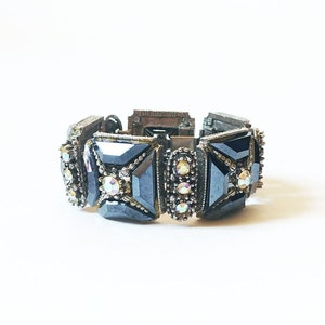 May include: A black bracelet with a geometric design and clear rhinestones. The bracelet is made of metal and has a clasp closure.