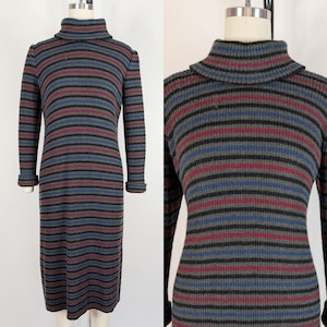Op de afbeelding: Een lange mouwen, knielange jurk met een coltrui. De jurk heeft horizontale strepen in grijs, zwart, blauw en bordeauxrood. De manchetten van de mouwen zijn omgeslagen. De jurk wordt op een mannequin gepresenteerd.