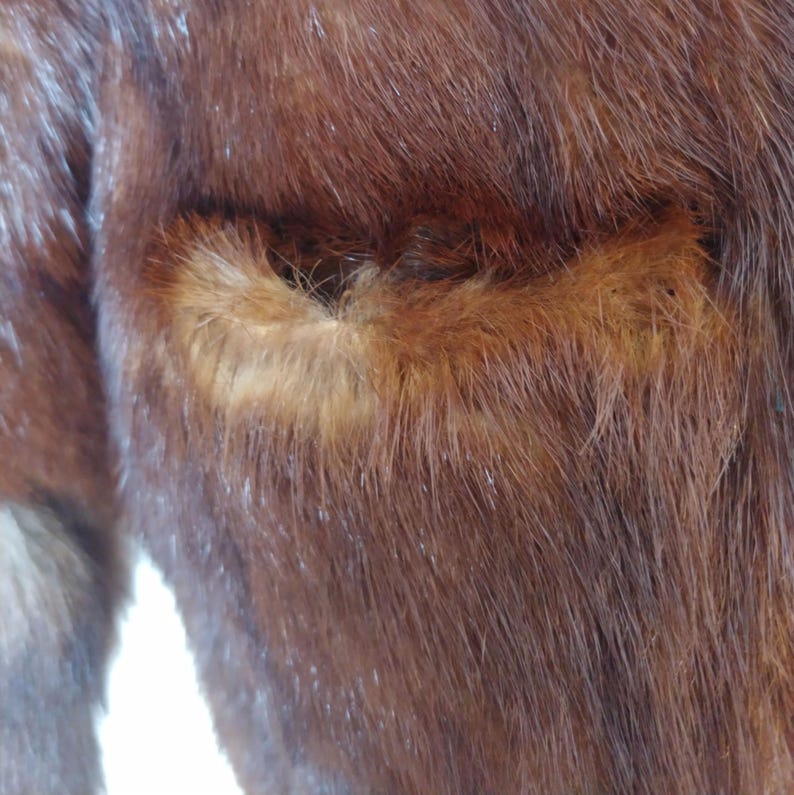 May include: Close-up of a brown fur coat with a pocket. The fur is a rich, dark brown color with lighter brown highlights. The pocket is outlined with a lighter shade of brown fur.