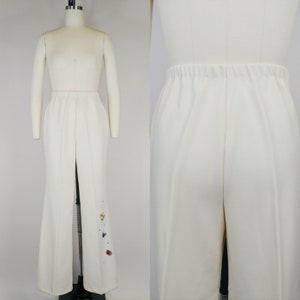 Peut inclure: Pantalon blanc &agrave; jambes larges avec une l&eacute;g&egrave;re &eacute;vas&eacute;e en bas. Le pantalon a un design simple et est d&eacute;cor&eacute; de petites fleurs brod&eacute;es color&eacute;es sur la jambe droite.