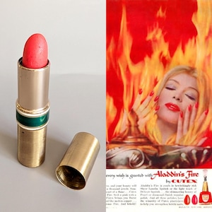 May include: A vintage lipstick with a coral bullet, in a gold-toned metal tube with a green band. The open tube and cap are visible. An advertisement for Cutex's Aladdin's Fire lipstick and nail polish is in the background.