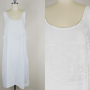 May include: White sleeveless dress with a white embroidered design on the front. The dress has a scoop neck and a loose fit.