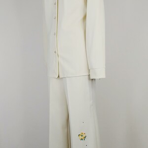 Peut inclure: Un tailleur pantalon blanc avec des papillons et des fleurs brod&eacute;s. La veste a un devant boutonn&eacute; et des manches longues. Le pantalon a une jambe large.
