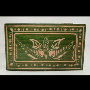Puede incluir: Una pequeña caja de madera con un exterior pintado de verde y un diseño floral tallado en un tono de verde más claro.