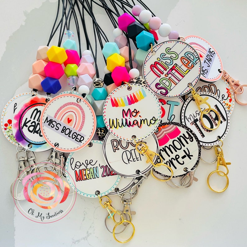 May include: A collection of colorful, personalized lanyards with various designs and text, including "Miss Bolger", "Mo Williamo", "Love Megan 2022", "Miss Spilled", "Harmony Pre-K", and "Rock Creek".