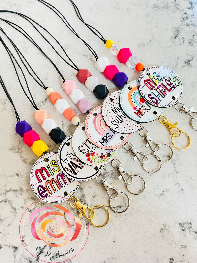 May include: A set of colorful teacher ID badge lanyards with colorful silicone beads and a variety of teacher name tags. The name tags feature a rainbow design and the text "Mrs. Shipley", "Mrs. Suthe", "Mis em VAY ST", "Mis em MRS. D".