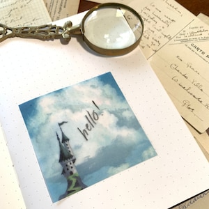 May include: A blue and white watercolor illustration of a castle with a flag that says "hello!" on it. The castle is in the clouds.