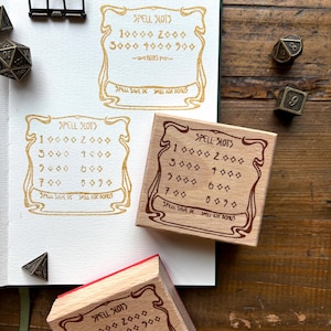 Puede incluir: Tres sellos de madera con marcos ornamentados y letras doradas. Los sellos son para rastrear espacios de hechizos, CD de salvación de hechizos y bonificación de ataque de hechizos en un juego de rol. El texto en los sellos dice "SPELL SLOTS", "SPELL SAVE DC" y "SPELL ATK BONUS".