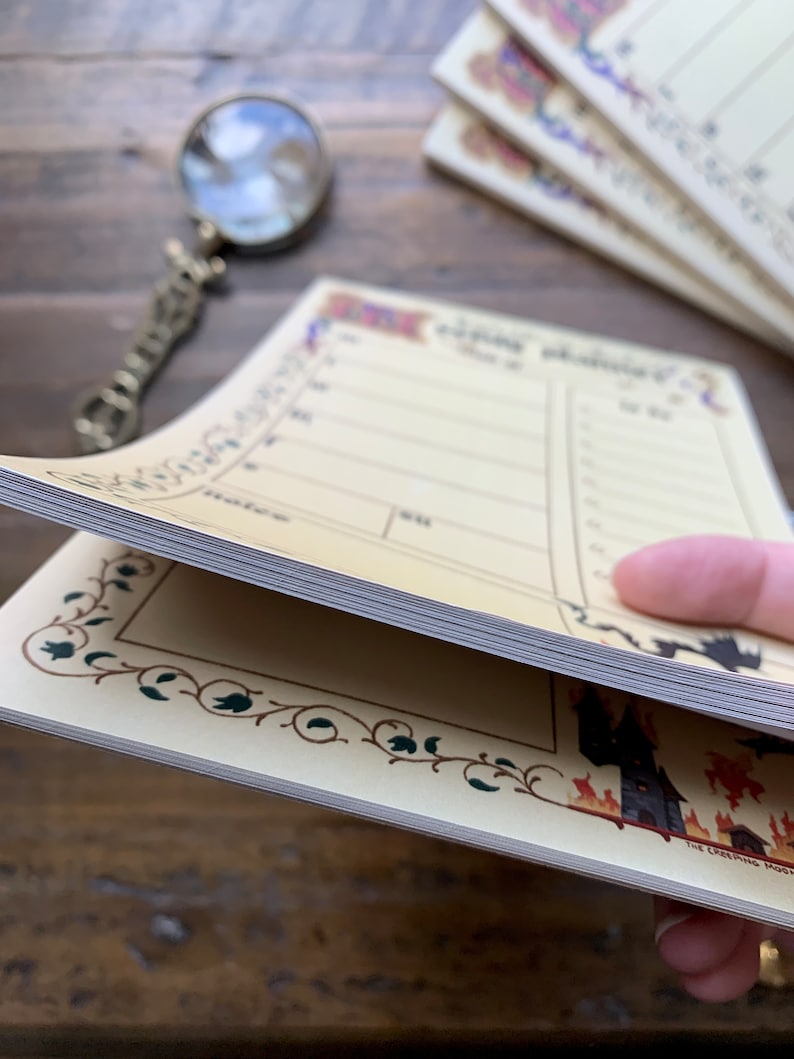 Pu&ograve; includere: Un blocco note giallo con un bordo decorativo e un'illustrazione in bianco e nero di una casa infestata. Il blocco note ha una sezione per "Da fare" e una sezione per "Note".