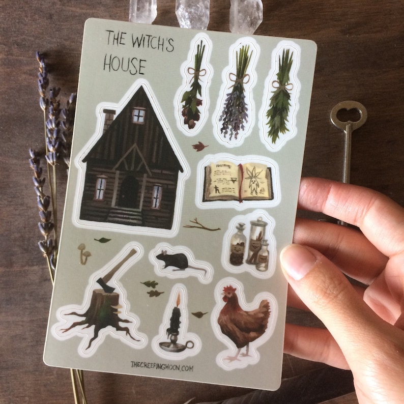 May include: A sheet of stickers featuring a witch's house, a book of spells, herbs, a rat, a chicken, a candle, an axe, and a key. The stickers are on a light green background with the text "The Witch's House" at the top.