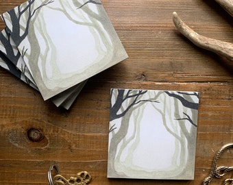 Puede incluir: Una pila de tarjetas de notas en blanco con una ilustración de acuarela de un camino en el bosque. Las tarjetas están sobre una superficie de madera con un par de llaves y un par de tijeras.