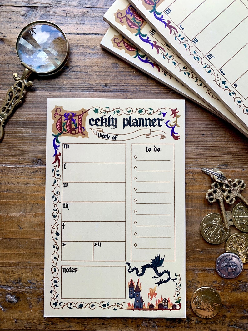 Pu&ograve; includere: Un blocco note per la pianificazione settimanale con un design in stile medievale. La copertina presenta un drago e un castello in fiamme. Il blocco note ha un elenco di cose da fare, una sezione note e un calendario settimanale.