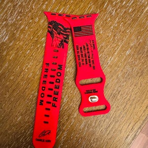 May include: Bright red Apple Watch band with black text and graphics. The band features the word "FREEDOM" in large letters, an American flag, and the text "THIS IS THE TURNING POINT". The band also includes the signature of Charlie Kirk.