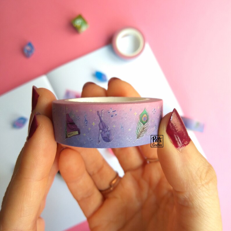 Close-up of a roll of washi tape with a pattern of Dungeons and Dragons elements on a purple background: book, violin, feather, flowers, etc