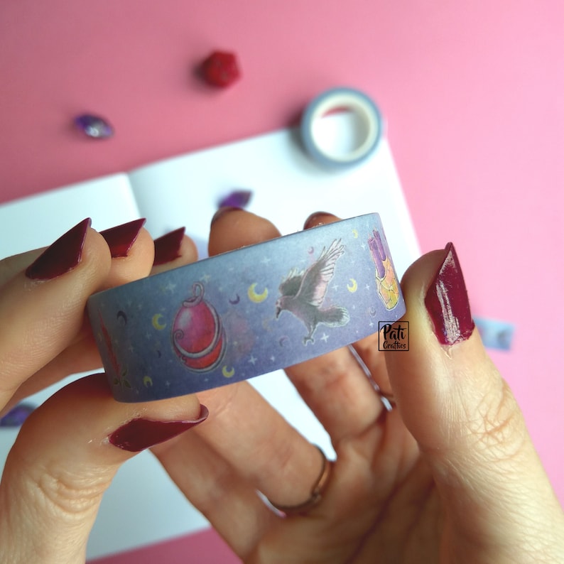 Close-up of a roll of washi tape with a pattern of Dungeons and Dragons elements on a purple background: amulet, crows, flowers and moons, etc