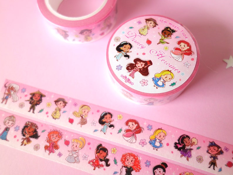 Washi tape with a pattern of mini Disney Princesses on pink background. Two rolls with their envelope, and two are extended showing characters like Kida, Raya, Jane, Aurora, Jasmine, Ariel, Alice, Esmeralda, Amelia, Elsa, Moana, Giselle...