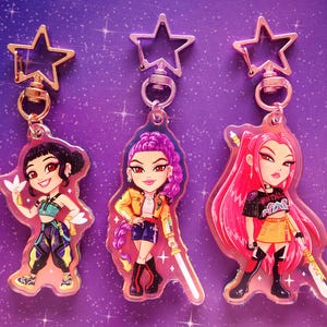 May include: Three acrylic keychains featuring anime-style illustrations of female characters. Each keychain has a star-shaped clasp. The characters have different hair colors and outfits, with one holding a sword. The background is a purple starry design.
