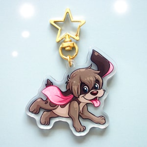 Puede incluir: Un perro de dibujos animados marrón y blanco con una capa rosa, corriendo y sacando la lengua. El perro está unido a un llavero en forma de estrella dorada.