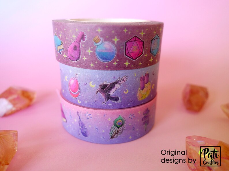 Washi tapes with a pattern of Dungeons and Dragons elements on a purple background. Three rolls are piled, one of each pattern.