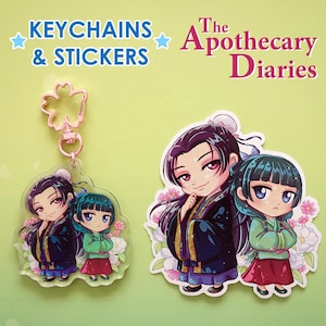 Puede incluir: Llaveros y pegatinas con ilustraciones de estilo anime de dos personajes de "The Apothecary Diaries". Un llavero tiene un cierre en forma de flor. Los personajes est&aacute;n representados con vestimenta tradicional.