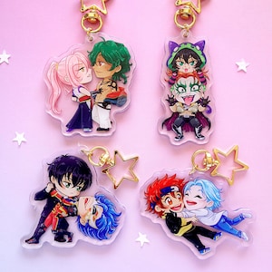 May include: Four acrylic keychains featuring anime-style characters in various poses. The keychains have gold-colored hardware and star-shaped charms. The characters have colorful hair and outfits, set against a pink background with white stars.