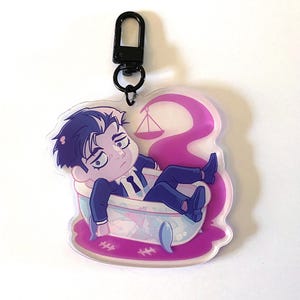 May include: An acrylic keychain featuring a cartoon character with dark hair wearing a blue suit, sitting inside a bathtub filled with purple liquid. A scale icon floats above the tub, and a black metal lobster clasp is attached to the top.