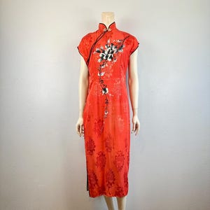 May include: A red silk cheongsam with a floral print and black trim. The dress has a mandarin collar and short sleeves.