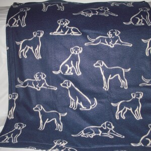 May include: A navy blue fleece blanket with a white silhouette pattern of Labrador Retrievers. The blanket is soft and cozy, perfect for cuddling up on the couch.
